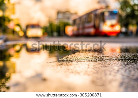 Sun after the rain in the city, view of the approaching tram with a level of puddles on the pavement