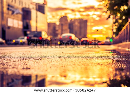 Sun after the rain in the city, view of the cars with a level of puddles on the pavement. Image in the yellow-purple toning