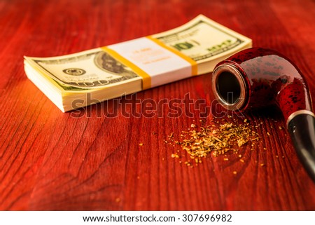 Tube for smoking tobacco and money on a wooden table. Focus on the tube