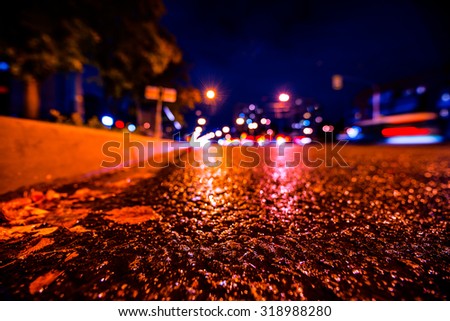 Rainy autumn night in the city, the glowing lights of approaching cars. View from the side of the road at the level of the asphalt, image in the blue toning