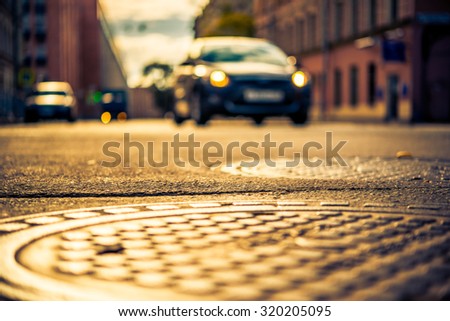 Autumn in the city, car driving on the street. View from the hatches on the pavement level, image in the yellow-blue toning