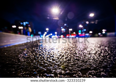 Night city after rain, the glowing lights of approaching cars. View from the side of the road at the level of the asphalt, in blue tones