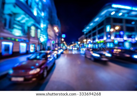 Nights lights of the big city, cars go down the avenue past the bright shop windows. Wide-angle view, defocused image, in blue tones