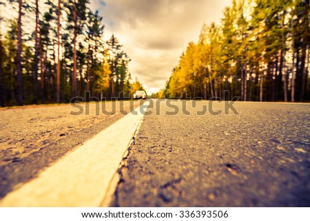 Autumn on the country road, the lights of the approaching car. View from the level of asphalt, image in the yellow-blue toning