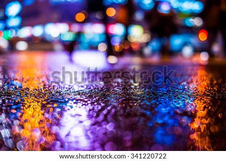 Rainy night in the big city, pedestrians cross the busy intersection in the light of shop windows. View from the level of asphalt