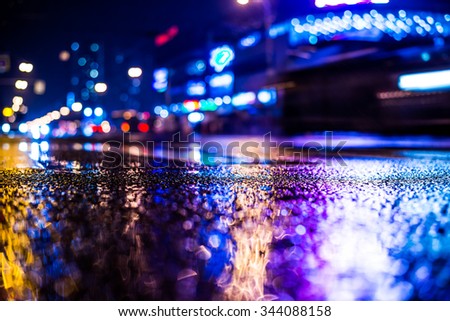 Rainy night in the big city, dense traffic on the avenue in the light of shop windows. View from the level of asphalt, in blue tones