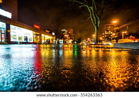 Rainy night in the big city, city street, in the light of shop windows. View from a wide angle at the level of asphalt