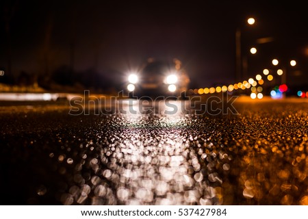 Rainy night in the big city, the car traveling towards the headlights illuminate the road. Close up view from the asphalt level