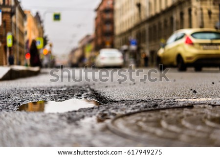 Rainy day in the big city, the cars drive along the old road. Close up view of a hatch at the level of the asphalt