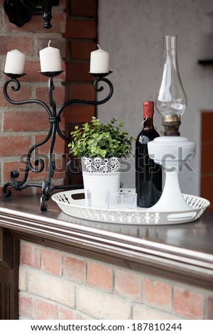 Moody ornamental arrangement with lamp, plant, candles and bottle of wine with brick texture in the background