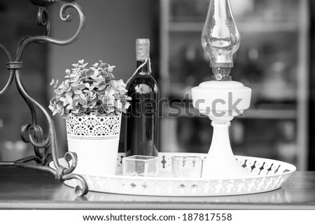 Black and white ,moody ornamental arrangement with lamp, plant, candles and bottle of wine with brick texture in the background