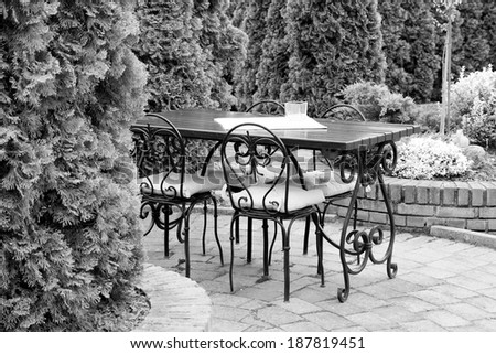 Black and white, moody ornamental arrangement with  candle  on a white table cloth on a wooden table with metallic chairs and green plants in the background