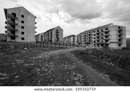 Black and white abandoned block of flats under construction with road leading to them.  Brick and cement textures with grass all around