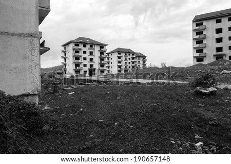 Black and white abandoned block of flats under construction with road leading to them. Brick and cement textures with grass all around