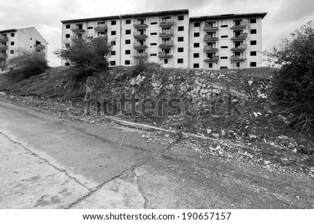 Black and white abandoned block of flats under construction with road leading to them. Brick and cement textures with grass all around