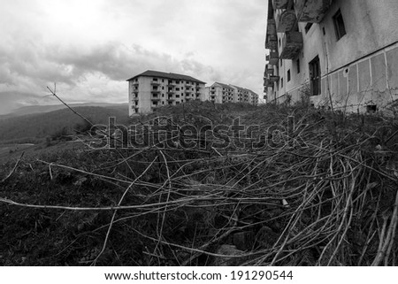 Black and white abandoned block of flats under construction with dried herbs and bushes