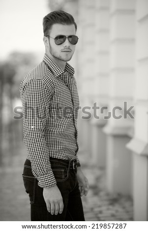 Black and white photo of a handsome young man wearing a shirt and jeans. Street shooting in Timisoara, Romania