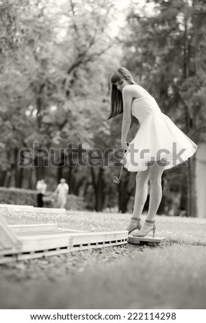 Black and white photo of a beautiful, caucasian, young, long haired woman posing in the park, wearing a white dress