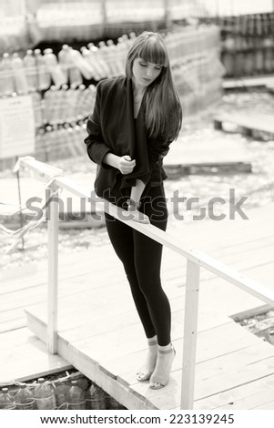 Black and white photo of a beautiful, caucasian, young, long haired woman posing in urban locations with plastic bottles construction