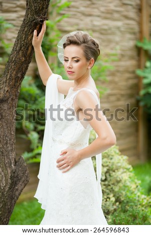 Beautiful, caucasian, brown haired woman wearing a wedding dress with natural, green background
