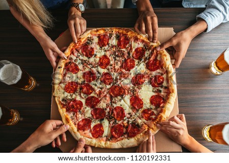 High angle shot of a group of unrecognizable people\'s hands each grabbing a slice of pizza