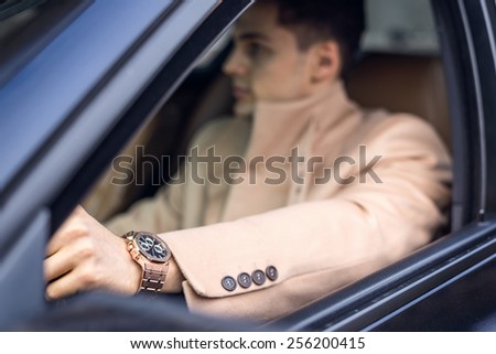 Handsome stylish male driving the car, focus on the watch (foreground). Natural light