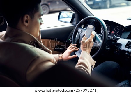 Stylish young man using mobile phone in the car. Soft focus on the phone and hands