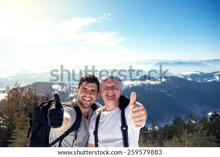 Cheerful young and middle aged man keeping thumb up on the top of the mountain. Direct sunlight, warmer highlights, shallow depth of field.