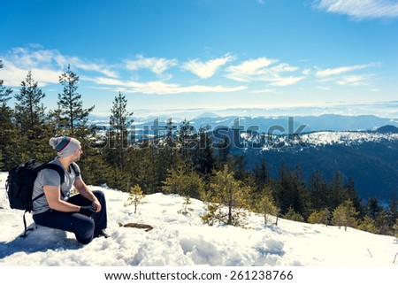 Young hiker sitting in the snow on the top of the mountain, looking away. Copy space on the right side of the frame, warmer tones in the highlights.
