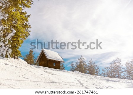 Small wooden house on he mountain covered with snow, Direct sunlight with lens flare from the right side of the frame. Copy space, toned image