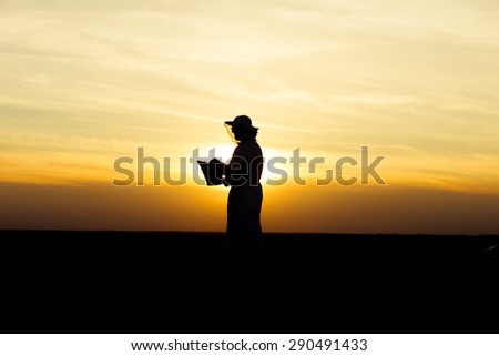 Apiarist silhouette in the field holding a smoker at sunset. Warm tones, sunlight