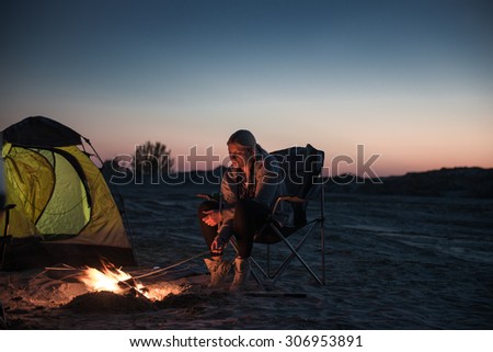 Young girl lighting a fire in front of the tent and a sky full of stars.