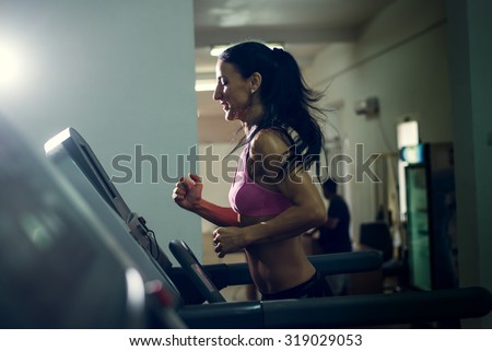 Shot of a girl running on the treadmill at their local gym. Dramatic light, selective focus, toned image.