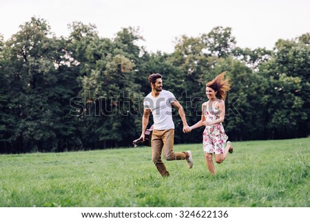 Shot of a young couple holding hands and running through the park. Blurry movement, soft focus.