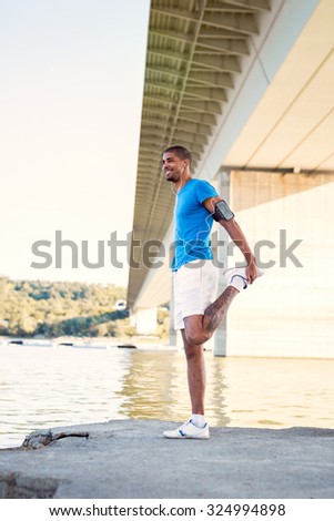Young male athlete stretching next to the river after morning work out.