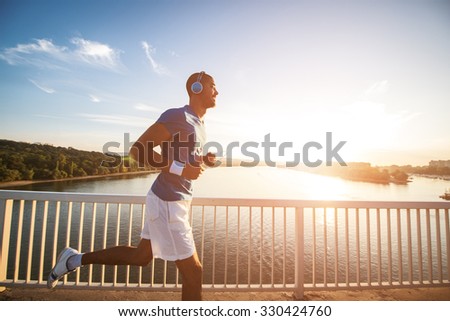 A young man running on the bridge along a river. Lens flare, warm tones.
