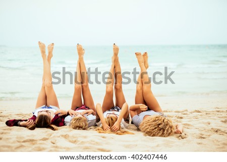 Attractive women lying down on the beach and putting their feet up.