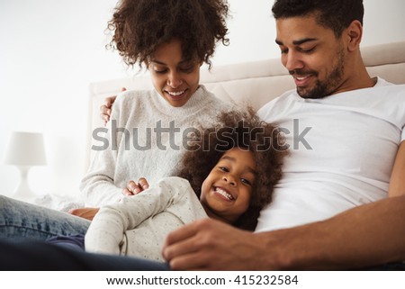 Shot of a laughing little girl lying in bed with her parents in the morning.