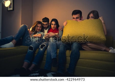 Friends watching a scary movie at home.