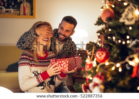 Handsome man surprising a girl with a Christmas present.