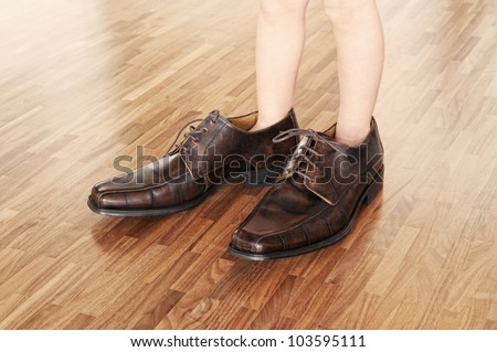 Big shoes to fill, child\'s feet in large brown shoes, on walnut parquet floor.