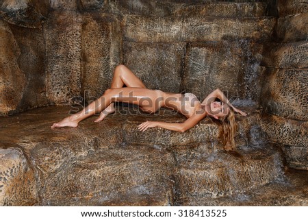 Beautiful blonde model wet sexy muscle woman lying on the mountains, the rocks at the waterfall flies on her water in a wet swimsuit erotic crystals lingerie in Santorini in Greece