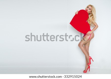 Beautiful blond sexy women model girl in love Valentine\'s Day with a red big heart to her face and red lips and red erotic lingerie long legs nude