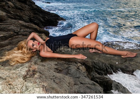 Beautiful blond hair sexy woman young girl model  elegant black and gold sexy swimsuit lingerie with tattoo overlooking  rough sea and the island on the rocks,storm, waves