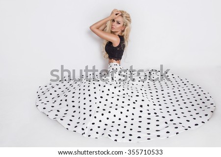 Beautiful blond with long curly hair young woman in the white model black ball gown, a polka color with a long train on a white background