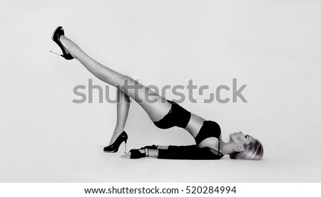 Beautiful woman with long blond hair lying on her back on the ground in sexy position with legs raised above the ground with a beautiful outdoor belly in black sexy dress and wearing the gloves