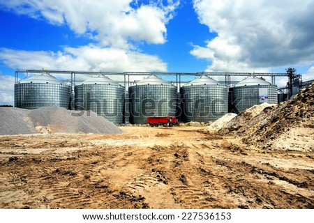 A row of granaries against the blue sky. Silos for wheat storage and drying. A red lorry in front of the granaries.