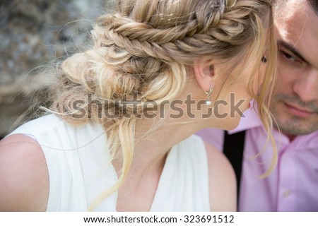 Bride and groom sitting in a large gray stone, the groom kisses the bride. Images of the newlyweds in the boho style, rustic. Hair girl in braids, ruffled by the wind. Close-up of people\'s faces.