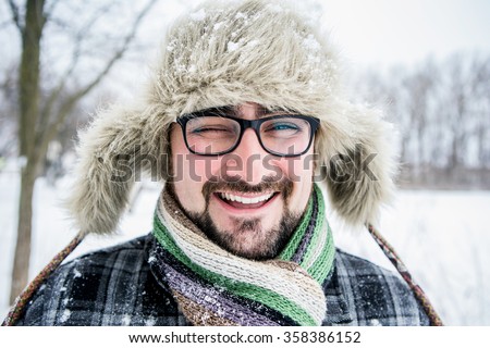 Adult man with beard wearing glasses. The man smiles. Winter, snow, a man in a fur hat. Man winks