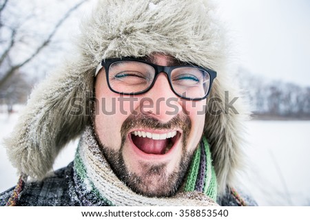 open-mouthed, adult man with beard wearing glasses.  Winter, snow, a man in a fur hat.
